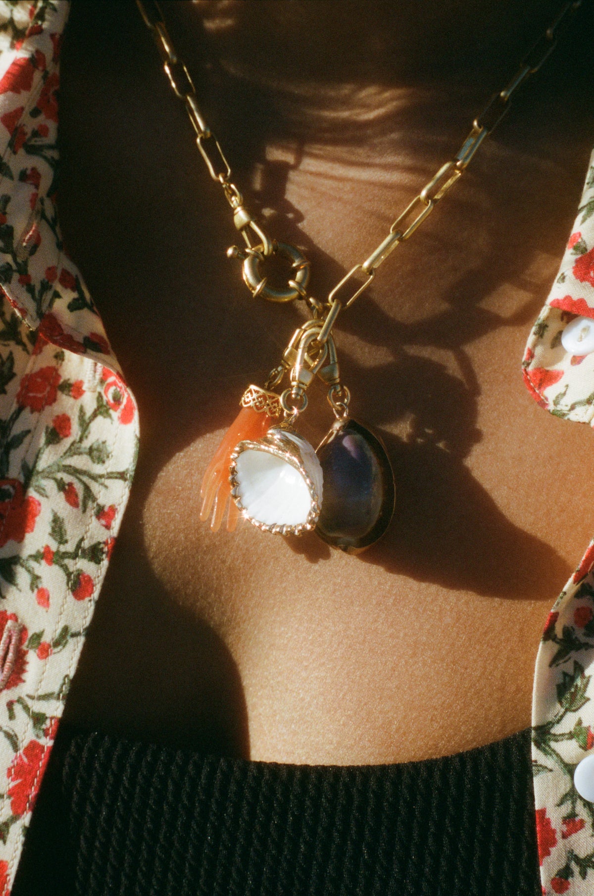 Close-up of a person wearing the Cowrie - Lavender gold chain necklace with three pendants, layered over a black textured top and floral shirt. A perfect accessory for lovers of bohemian jewellery.