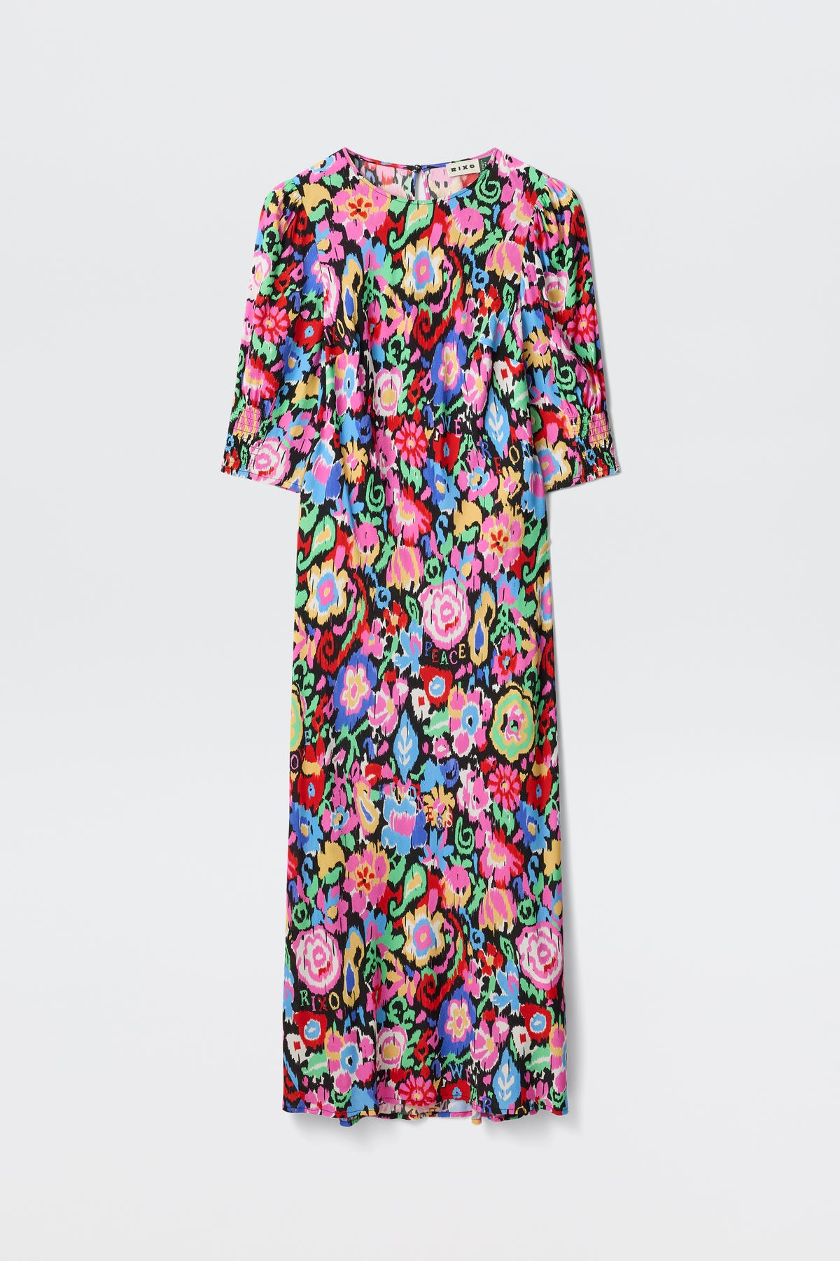 The Jess - Ikat Bloom Charcoal is a knee-length dress with short sleeves, showcasing a vibrant multicolored floral pattern on a black background. Flowers in pink, red, blue, green, and yellow stand out against a plain white backdrop.
