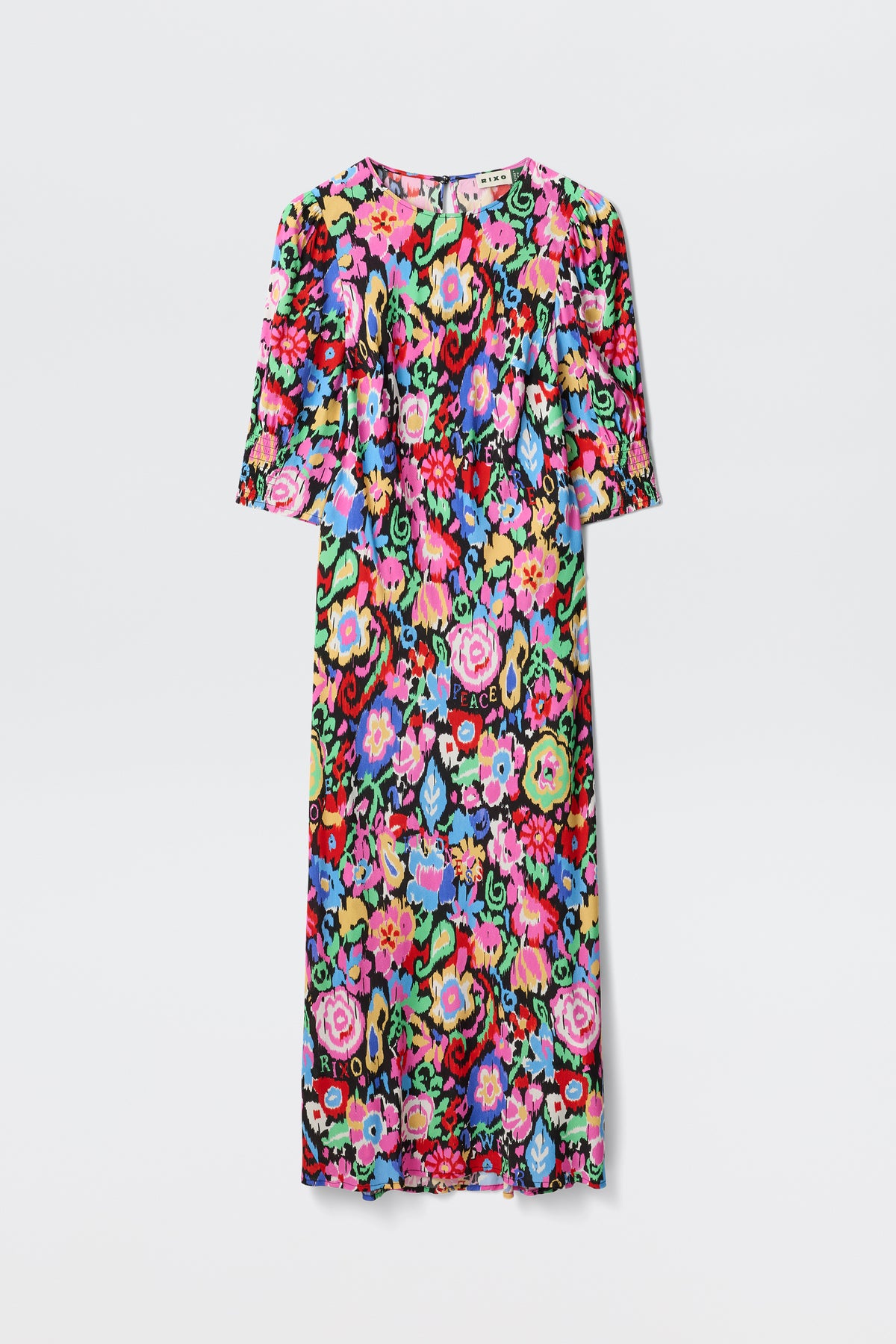 The Jess - Ikat Bloom Charcoal is a knee-length dress with short sleeves, showcasing a vibrant multicolored floral pattern on a black background. Flowers in pink, red, blue, green, and yellow stand out against a plain white backdrop.