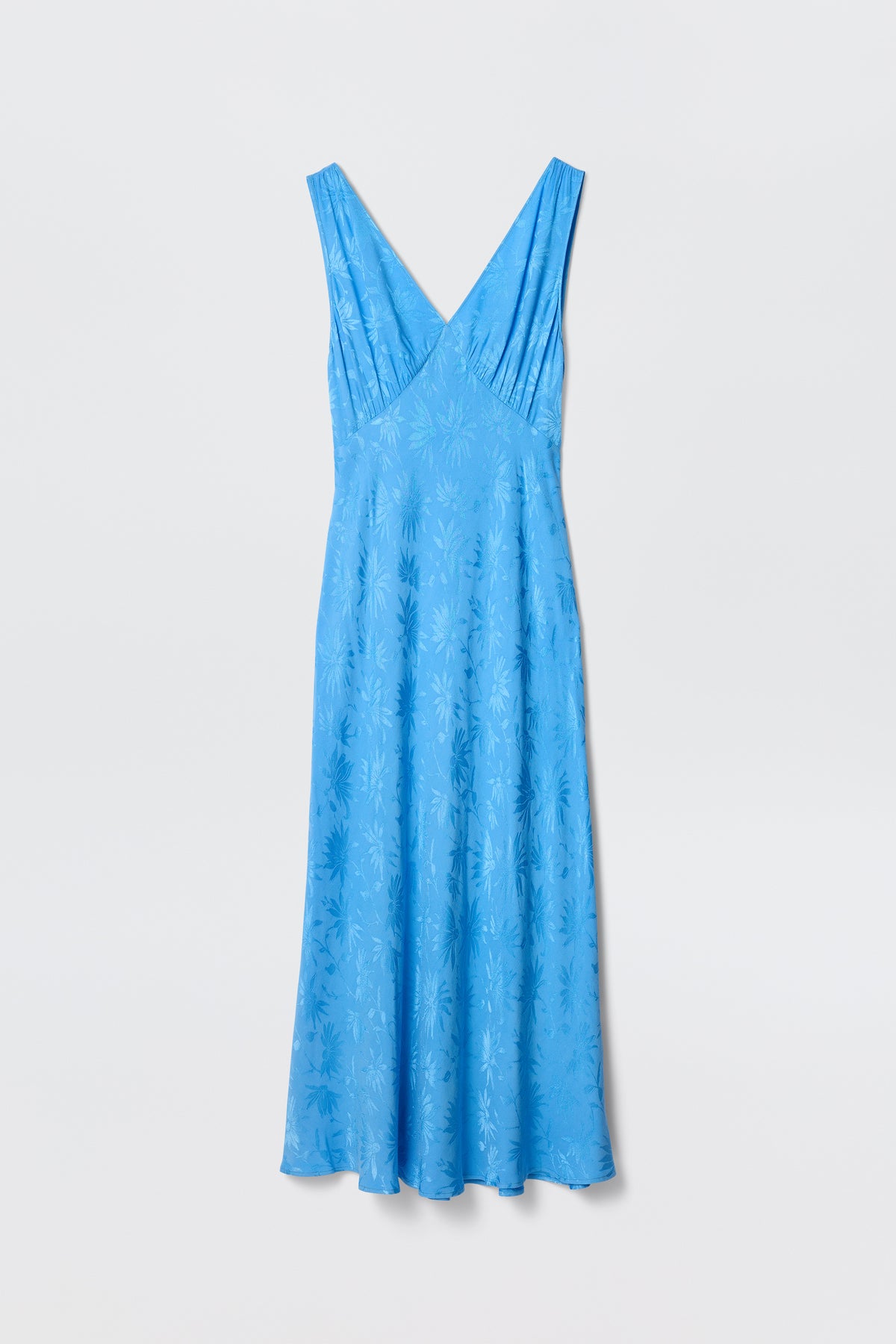 The Sandrine - Daisy Jacquard Blue by RIXO is a sleeveless, light blue V-neck midi slip dress with a subtle daisy jacquard pattern, shown on a plain white background.