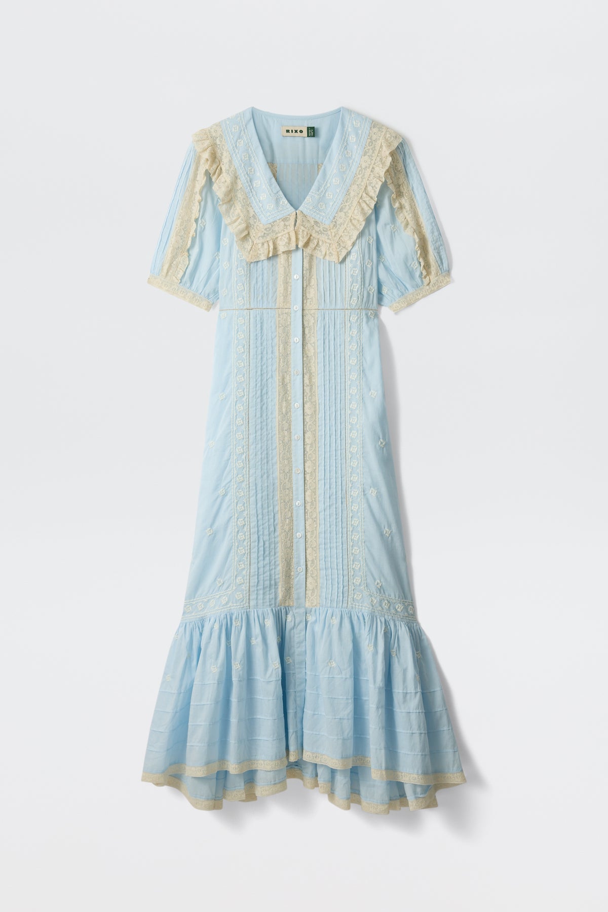 The Edina - Mira Embroidery Powder Blue is a light blue, short-sleeved midi dress with cream lace trim, ruffled collar, button-down front, decorative embroidery, and a flared hemline inspired by a powder blue blouse.