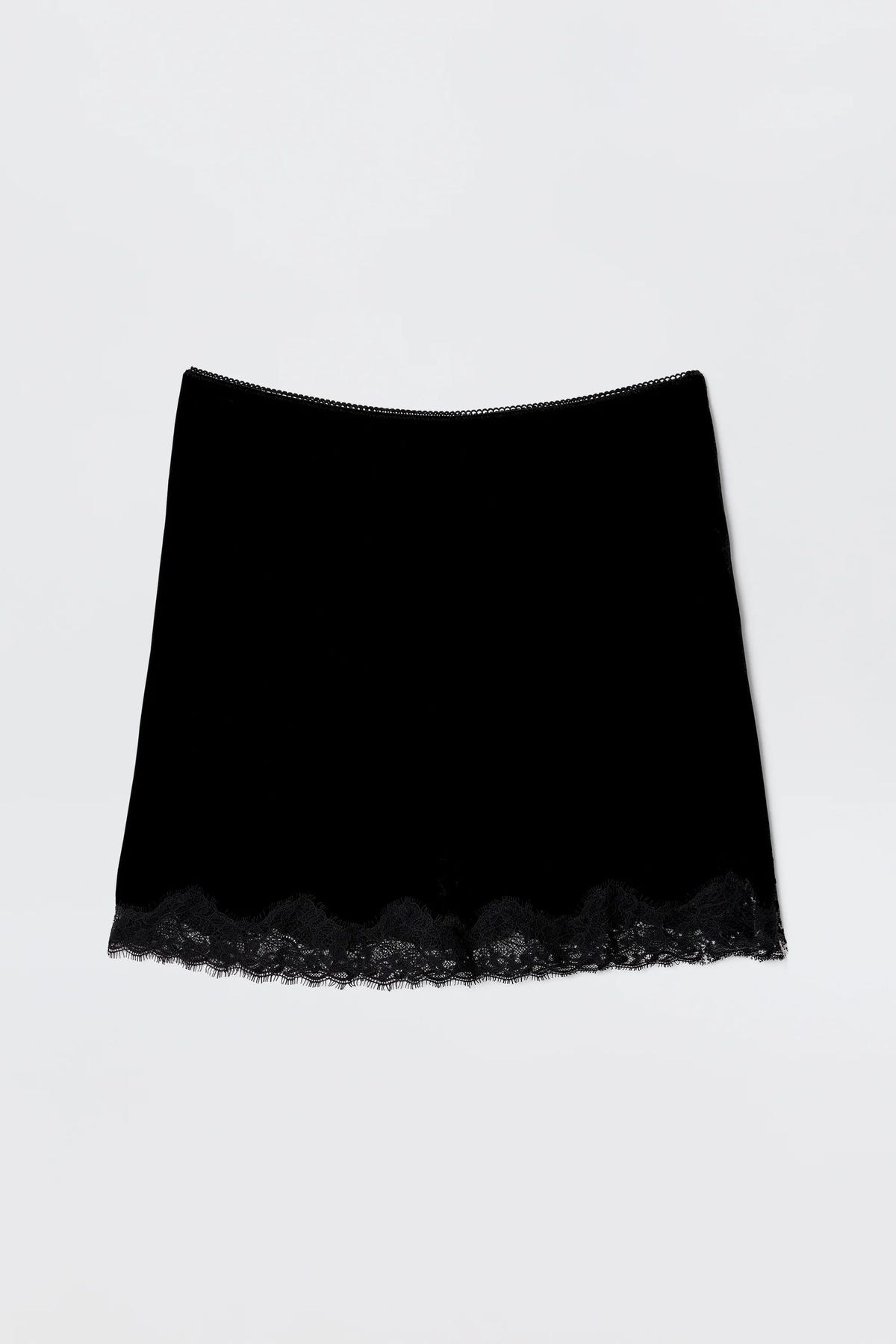 The Kornelia - Black is a nineties-inspired black velvet mini skirt with a straight fit and delicate lace trim at the hem, shown against a plain light background.