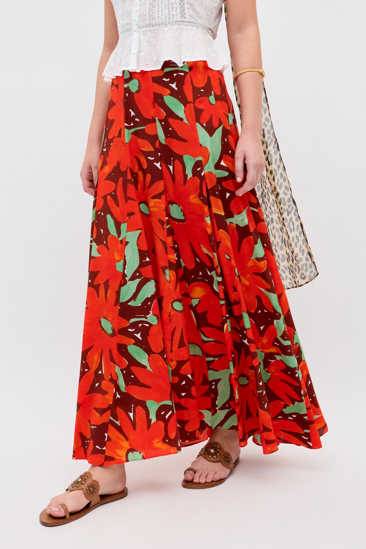Only the lower half of a person is visible, wearing the Billy - Danish Floral Orange skirt with a bold, colorful floral pattern, paired with brown sandals and a gold bracelet.