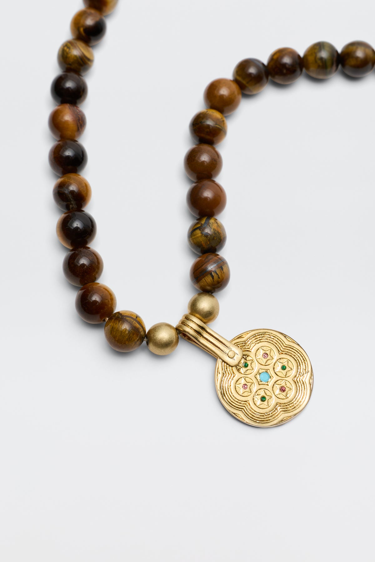 The Ischia - Brown necklace features round brown tiger's eye beads and a large ornate gold pendant with colorful accents, elegantly displayed against a plain light background.