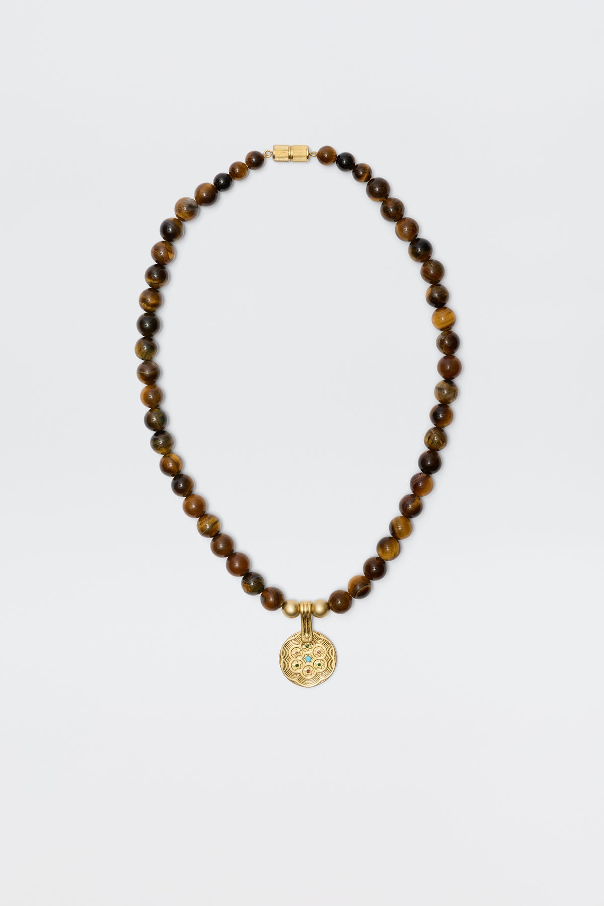 The Ischia - Brown necklace features round tiger's eye beads and a gold clasp, accented with a detailed circular gold pendant, shown on a plain white background.