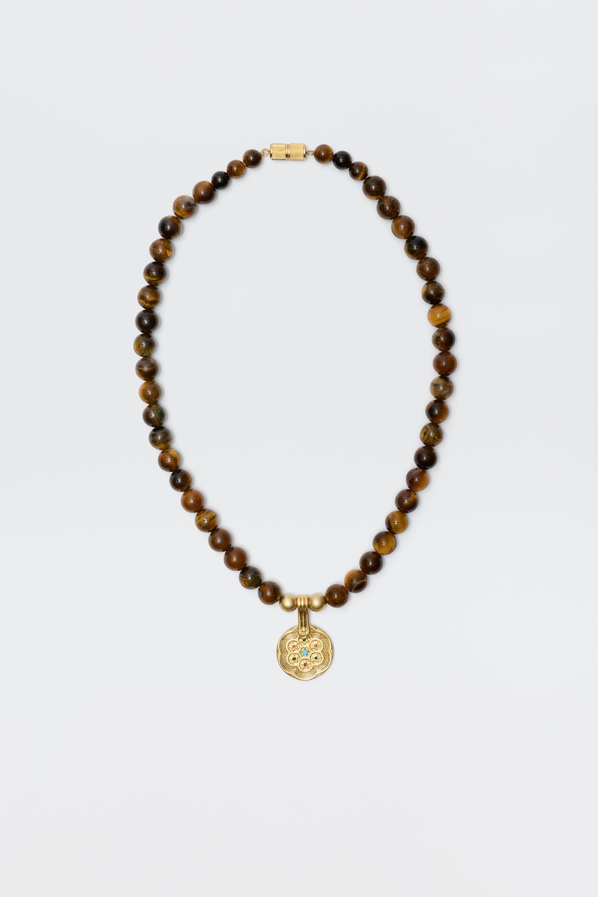 The Ischia - Brown necklace features round tiger's eye beads and a gold clasp, accented with a detailed circular gold pendant, shown on a plain white background.