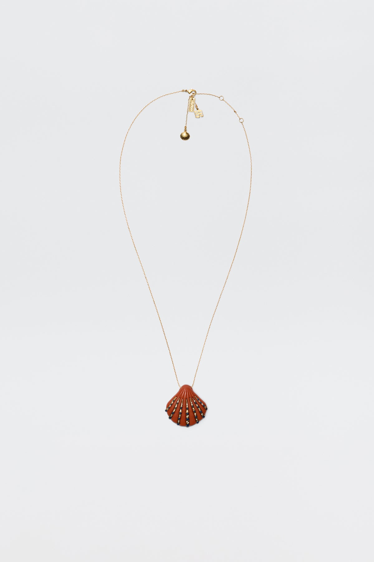 The Leanira - Orange necklace features a scallop shell-shaped pendant with small decorative studs on a gold-plated chain, shown against a plain white background.