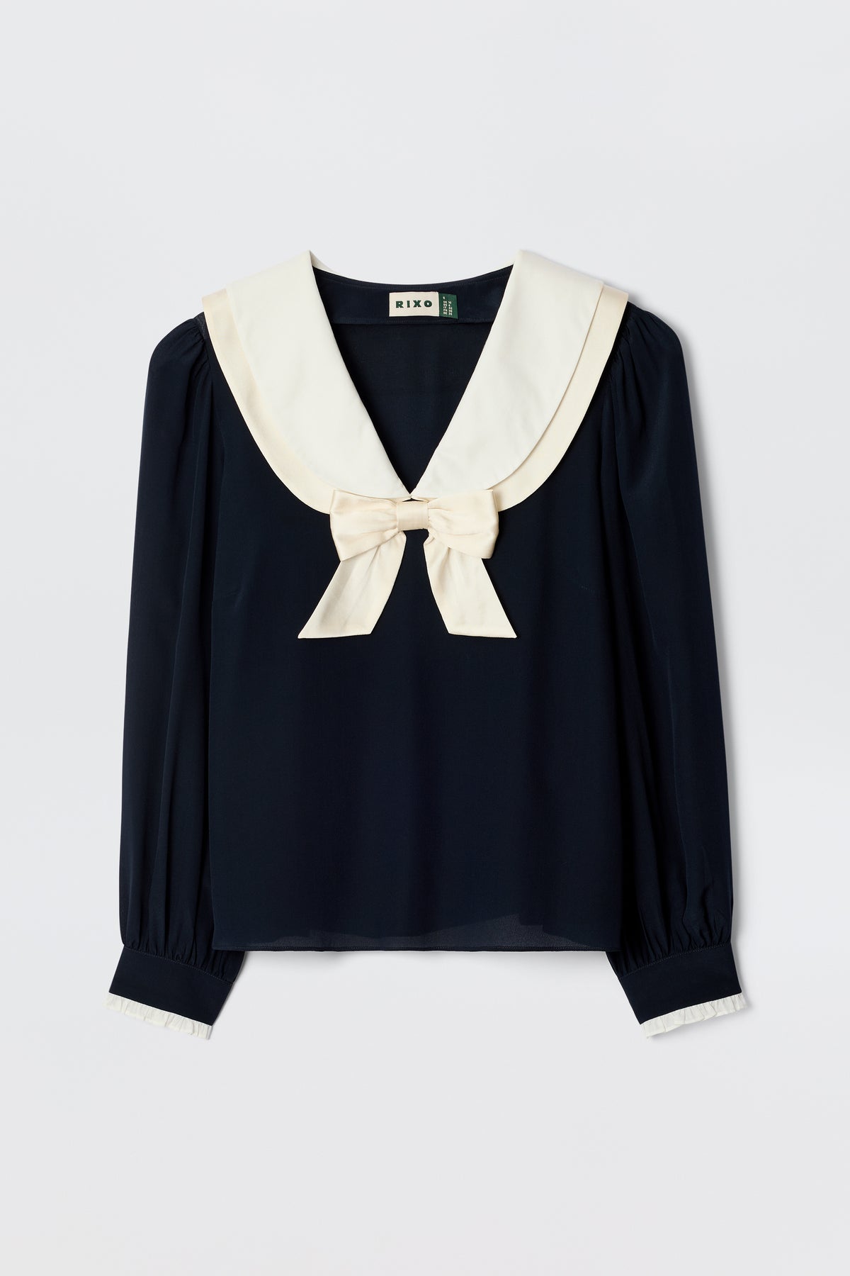 The Eimer - Navy is a long-sleeve silk top in navy with a large white sailor collar and matching bow. Featuring white-accented collar and cuffs, this classic blouse offers a relaxed fit for timeless style.