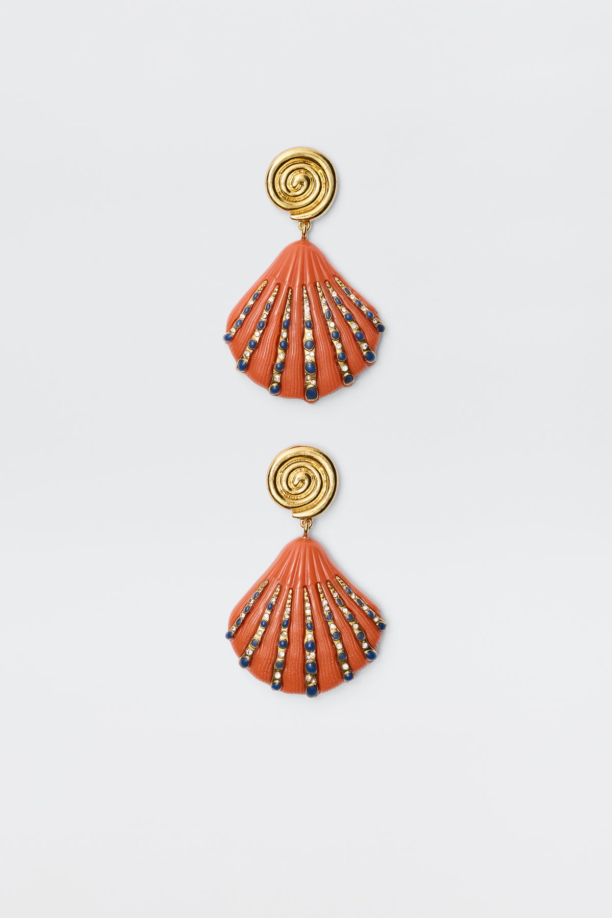 Daphne - Orange earrings feature gold spiral studs with orange-red shell-shaped pendants accented by blue, gold, and black beads, shown on a white background.
