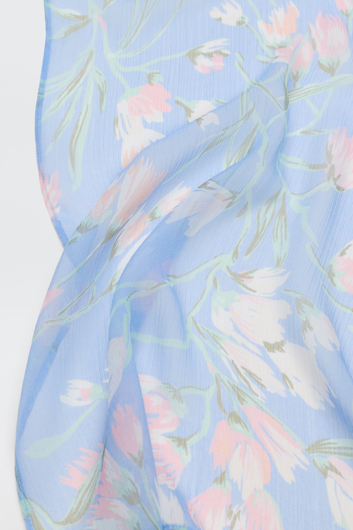 A close-up of Julien - Watercolour Floral Blue, a light blue sheer fabric featuring delicate floral patterns in soft pink, white, and green tones, draped to highlight its texture and translucency.