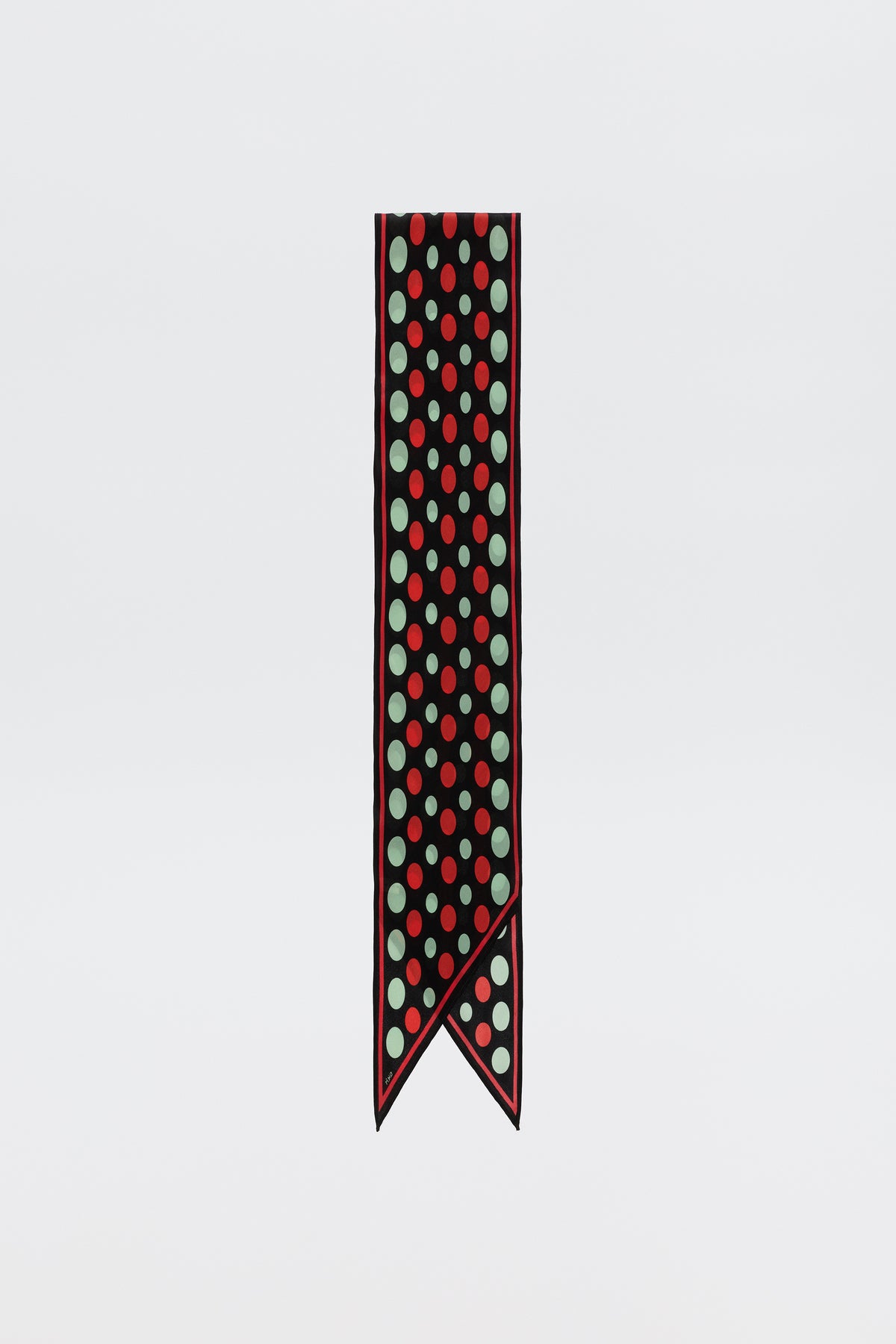 The Nara - Oval Spot Black scarf is a pure silk accessory with a narrow, pointed end, featuring large red and mint green polka dots on a black background, accented by thin red and white borders—an elegant piece shown on a plain white backdrop.
