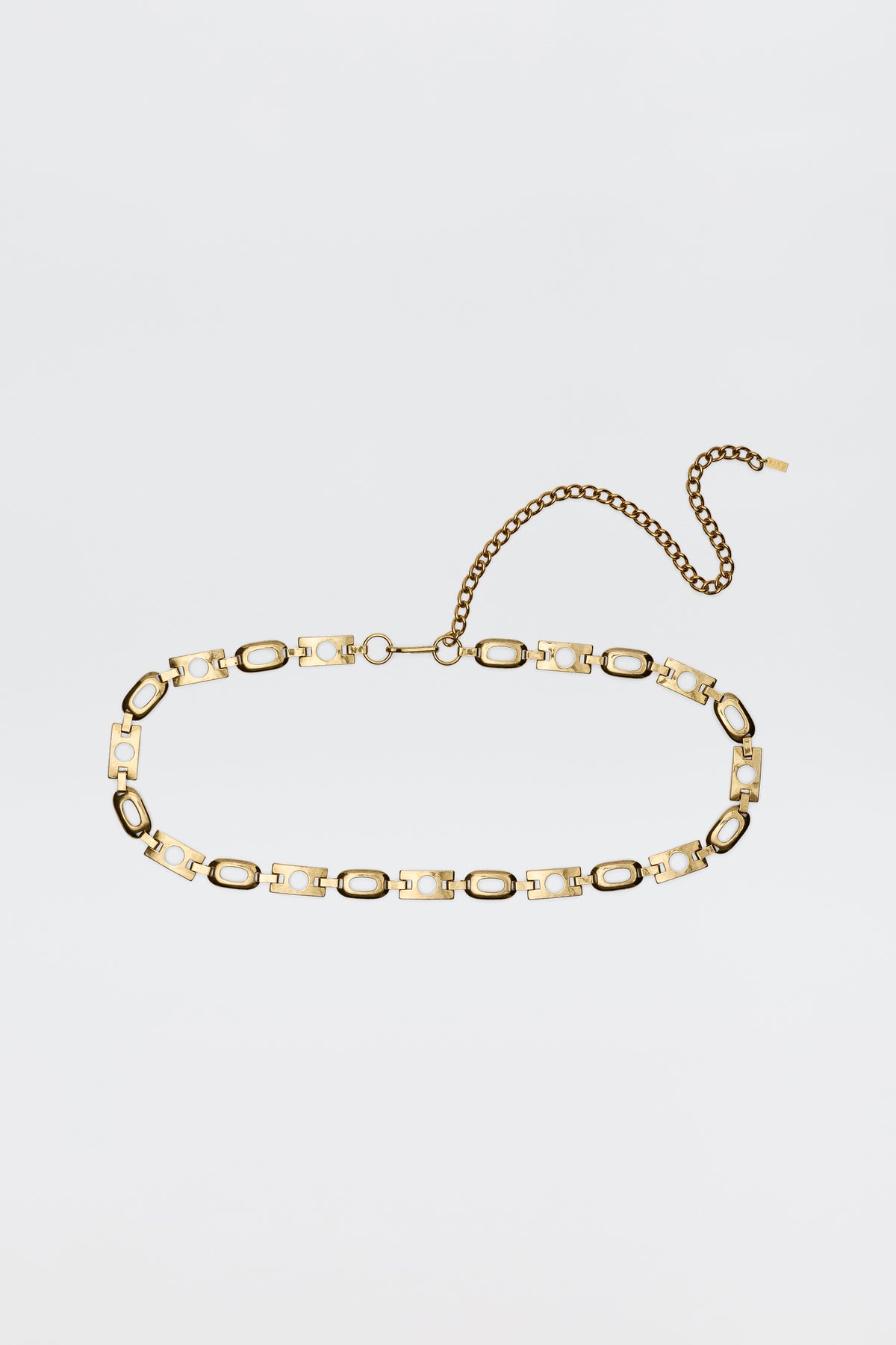 The Novie - Gold belt features alternating oval and rectangular gold-tone links, a lobster clasp, and an adjustable extension chain, displayed on a plain white background.