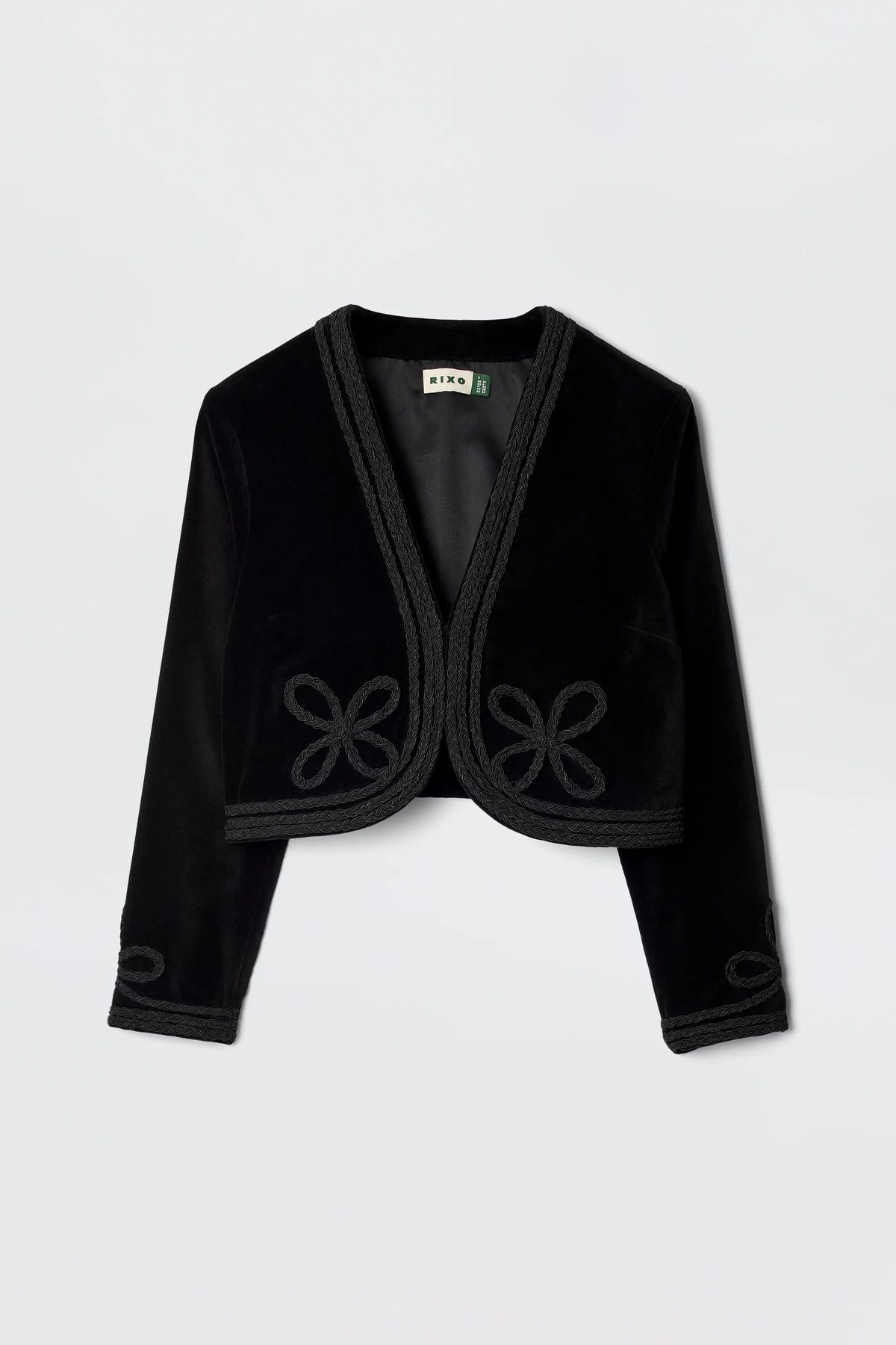 The Kesia - Clover Appliqué Black is a vintage-inspired cropped black velvet jacket featuring long sleeves, decorative trim, and knotted detailing on the front and cuffs, shown against a plain white background.