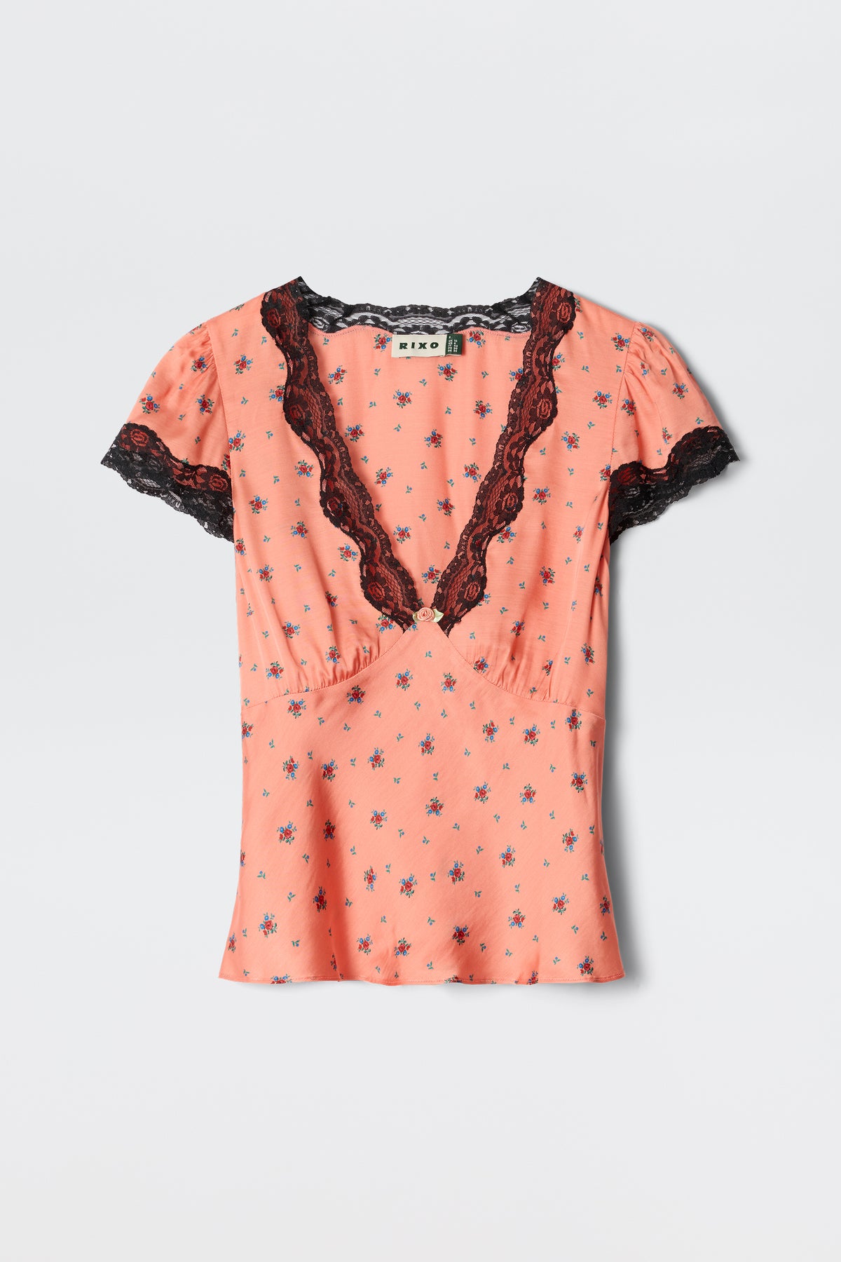 The Karia Peonies Ditsy Coral blouse features short sleeves, a deep V-neck with black lace trim, and a small floral pattern in coral tones, shown on a plain white background.