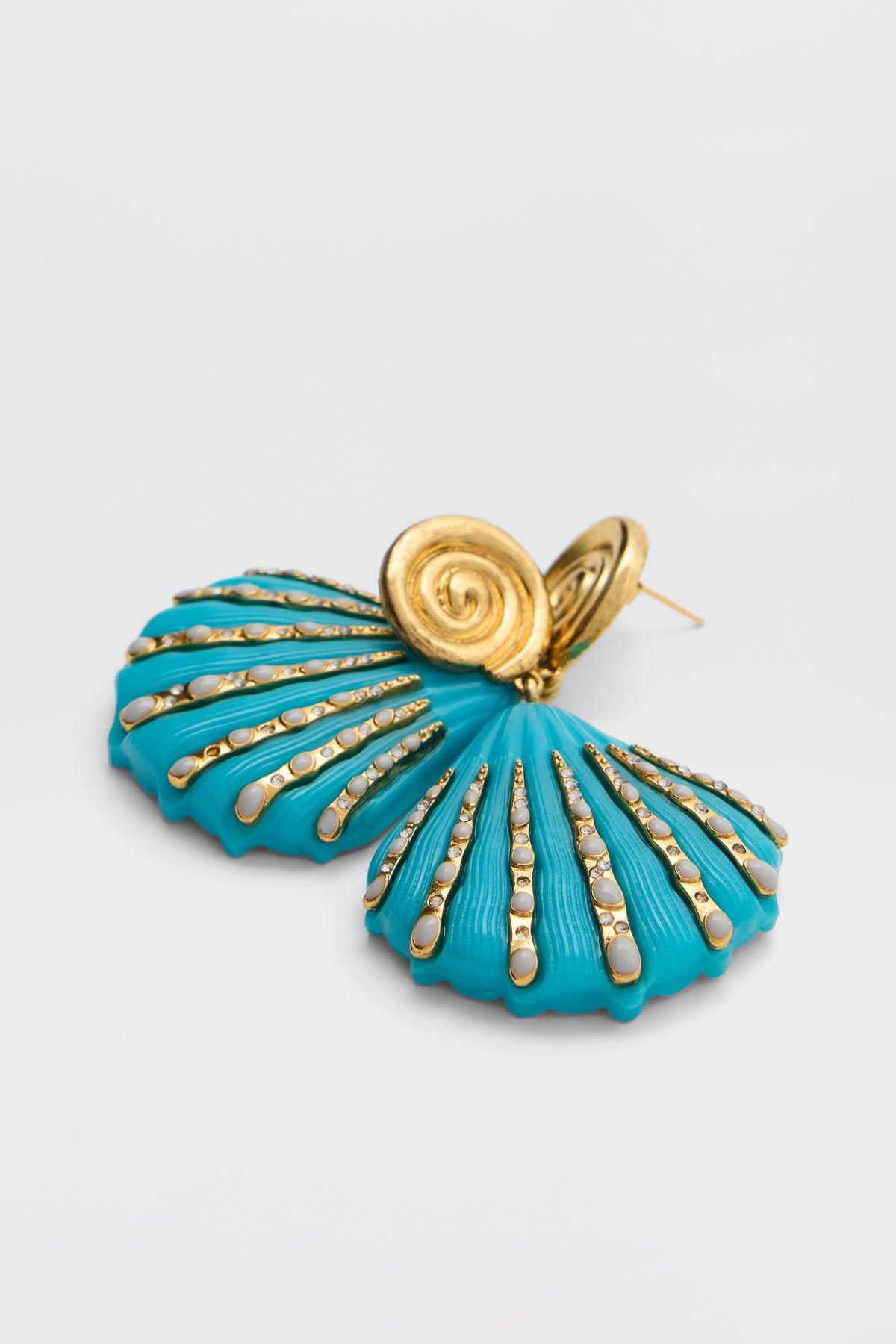 The Daphne - Turquoise earring features a gold and turquoise seashell shape with gold spiral and bead accents, shown on a light gray background.