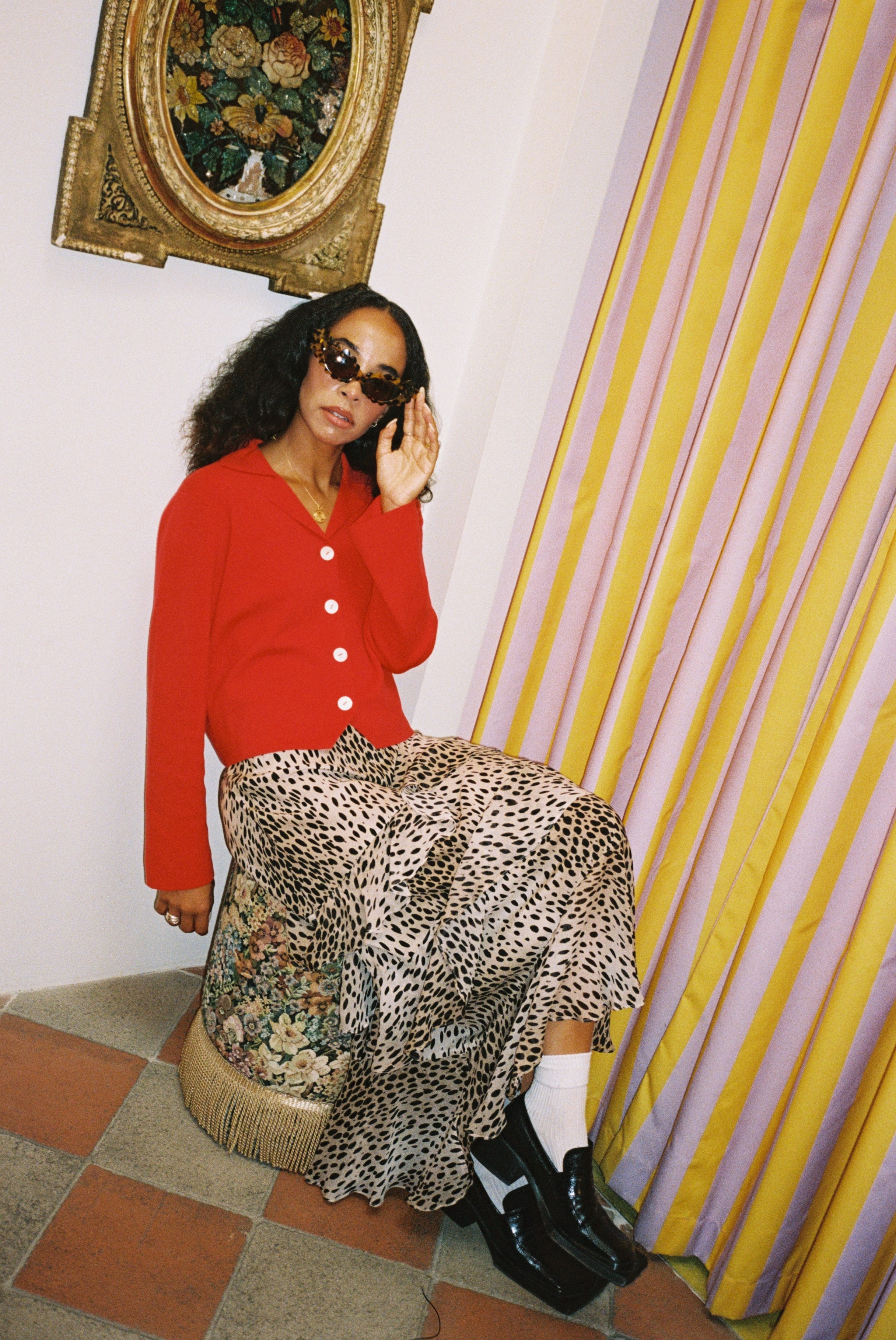 Person wearing a red cardigan and leopard print skirt in a room with a yellow curtain and decorative wall piece.
