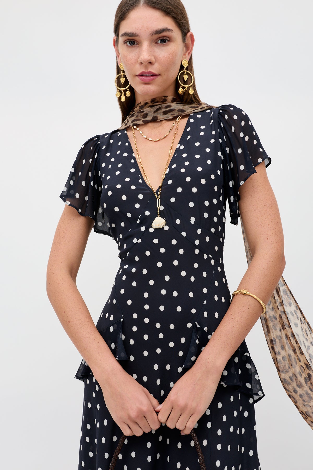 Woman wearing the Evie - Bohemia Spot Deep Navy dress, gold jewelry, and a sheer leopard-print scarf draped around her neck, standing against a plain light background.