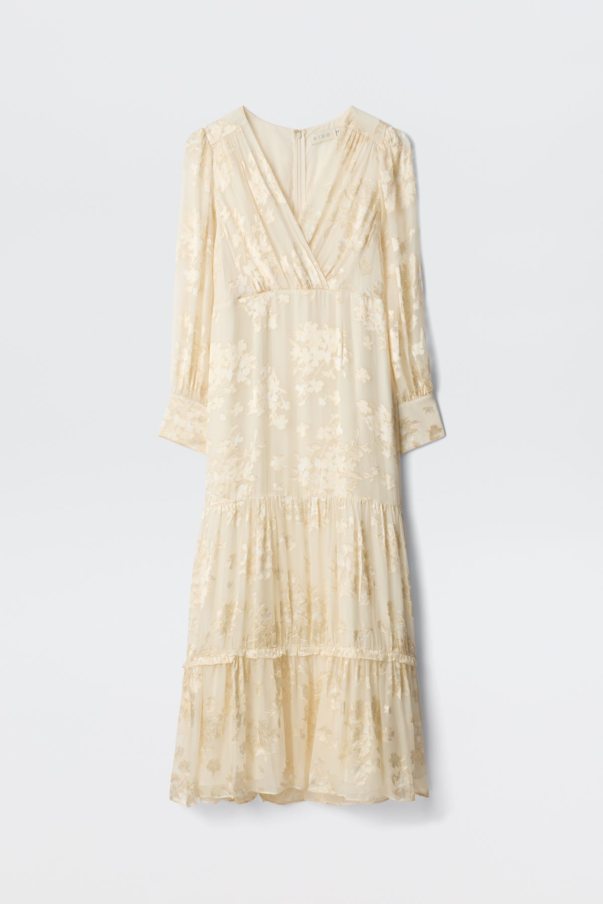 The Elsie - Bouquet Devore Cream is an ankle-length, cream dress with long sleeves, subtle floral pattern, V-neck, gathered waist, tiered skirt, and delicate pleats, shown on a plain white background.