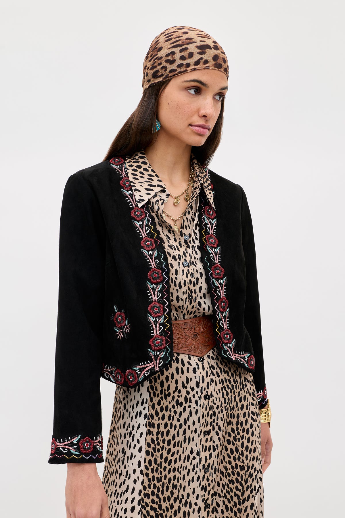 Woman wearing the Oliwia - Roselle Embellishment Black jacket over a leopard print dress and headscarf, styled with a brown belt, green earring, and gold necklace, standing against a plain light background.