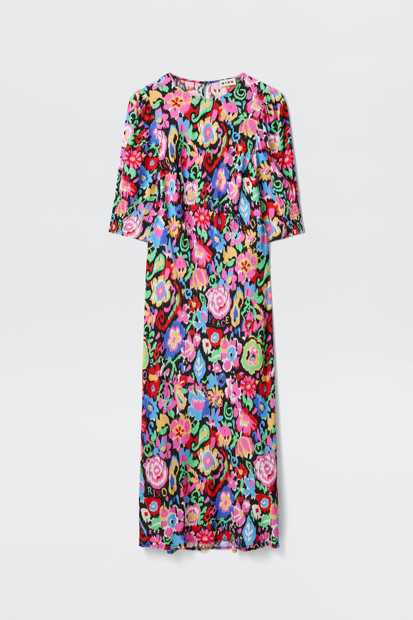 The Jess - Ikat Bloom Charcoal is a knee-length dress with short sleeves, showcasing a vibrant multicolored floral pattern on a black background. Flowers in pink, red, blue, green, and yellow stand out against a plain white backdrop.