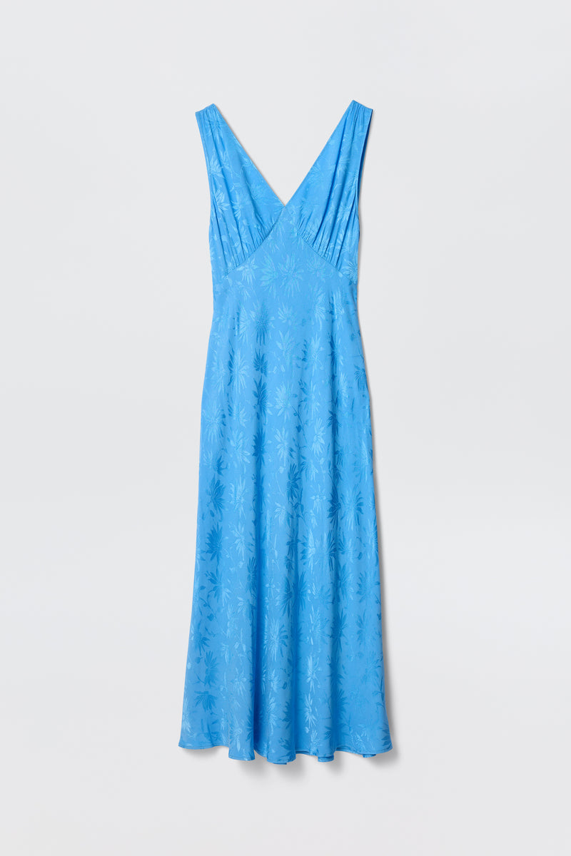 The Sandrine - Daisy Jacquard Blue by RIXO is a sleeveless, light blue V-neck midi slip dress with a subtle daisy jacquard pattern, shown on a plain white background.