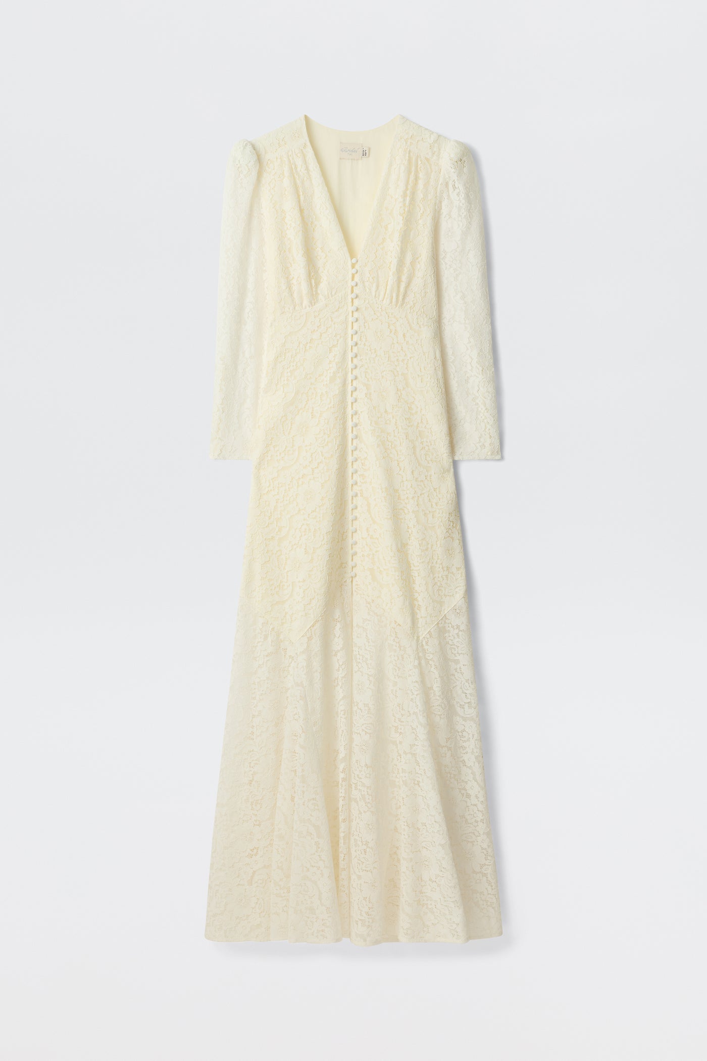 The Fleur - Ivory is a long-sleeved, floor-length ivory corded lace dress with a V-neckline, covered front buttons, and a subtle fit-and-flare silhouette, shown on a plain white background.