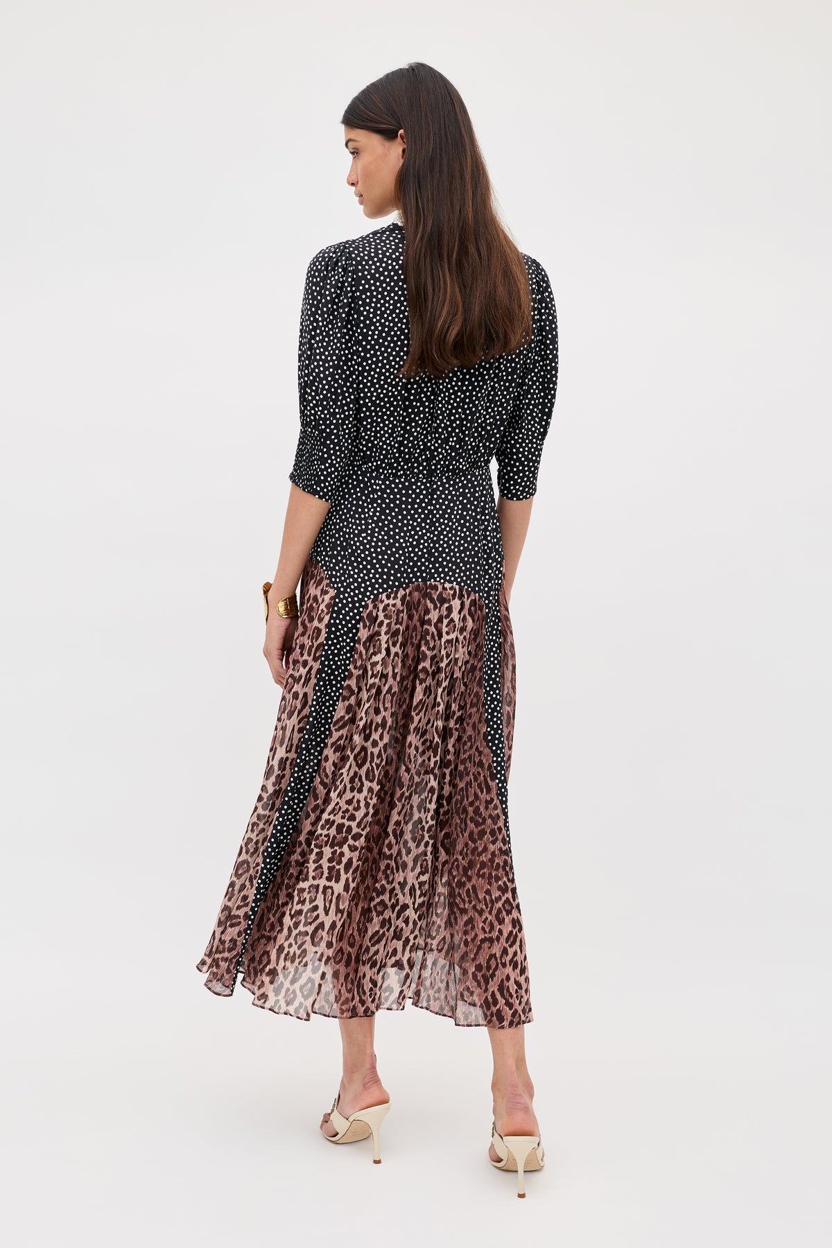 A woman faces away, wearing the "meg - leopard polka dot" dress with a fitted black and white polka dot top, flowing leopard print midi skirt, and light heeled sandals against a plain background.