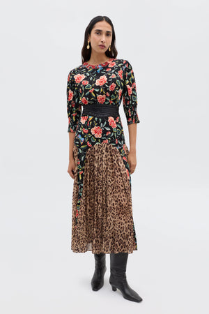 A woman stands against a plain background, embodying relaxed everyday style in the Meg - Mila Butterfly Mix Black dress by RIXO, styled with a black belt, gold earrings, and black knee-high boots.