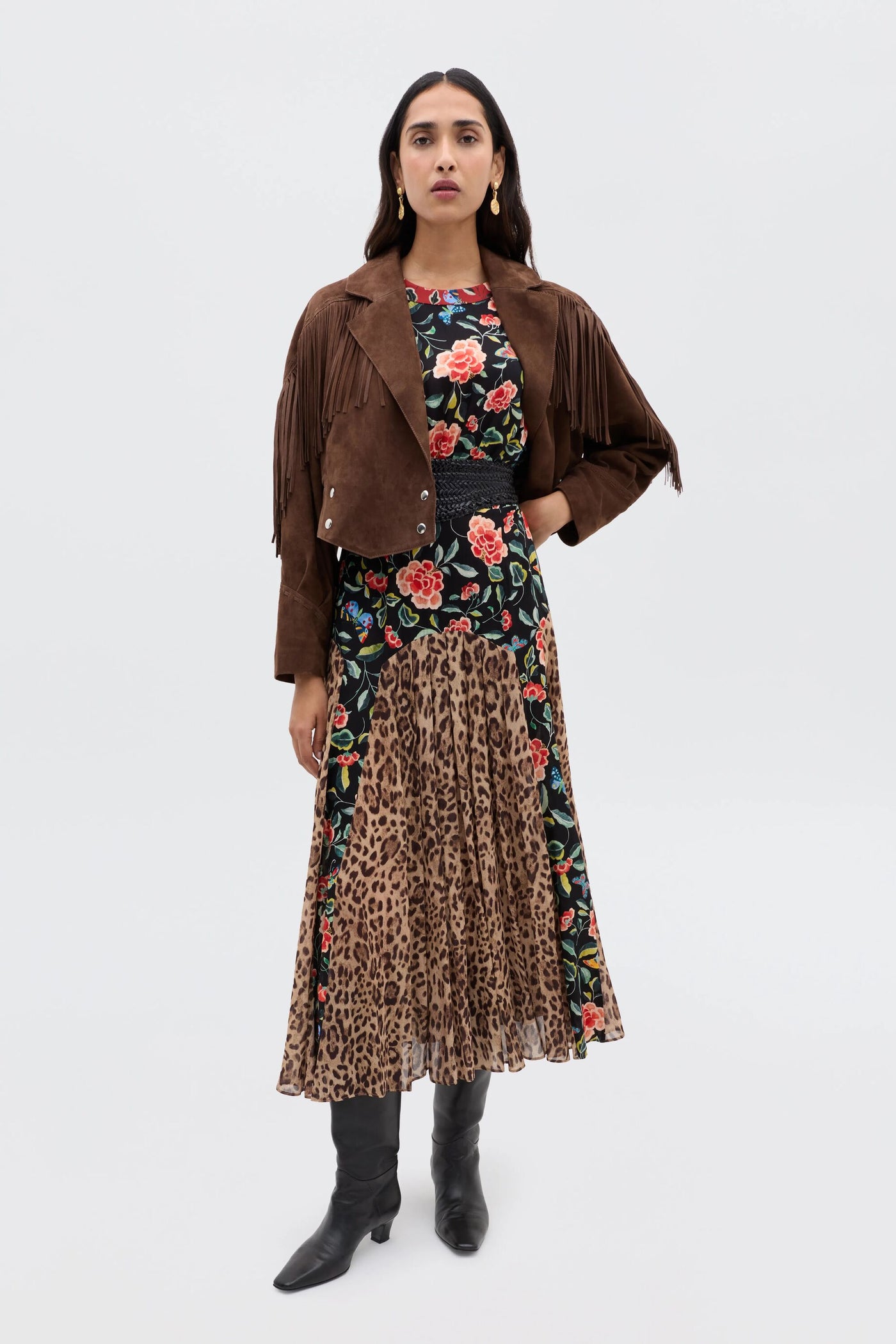 A woman stands against a plain background wearing a brown suede jacket with fringe, the RIXO Meg - Mila Butterfly Mix Black dress in contrasting prints, black knee-high boots, long dark hair, and gold hoop earrings—perfect for relaxed everyday style.