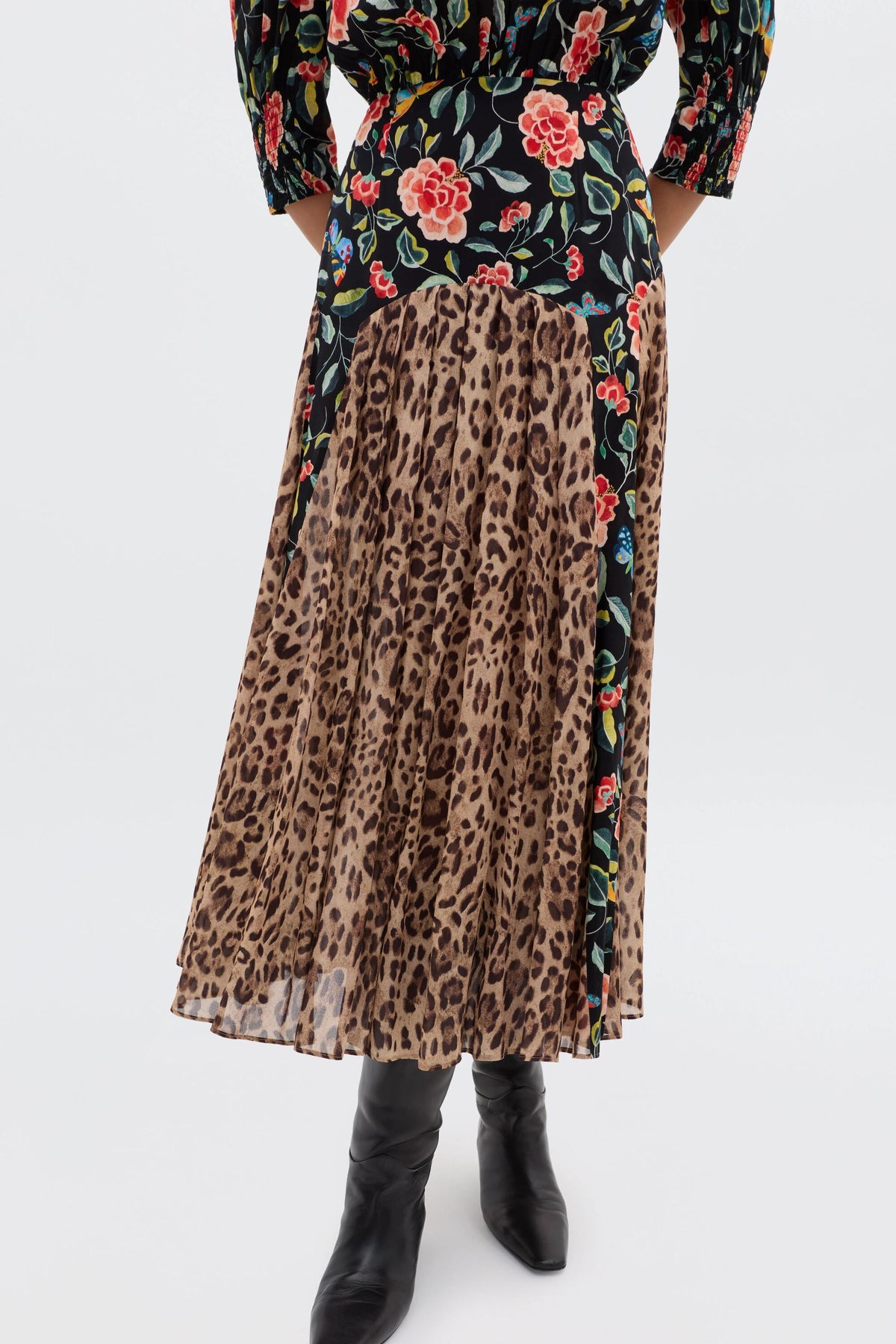A person displays relaxed everyday style in a black floral blouse tucked into the RIXO Meg - Mila Butterfly Mix Black high-waisted, pleated midi skirt with black knee-high boots; the mix of patterns adds effortless flair. Only the body is shown, not the face.