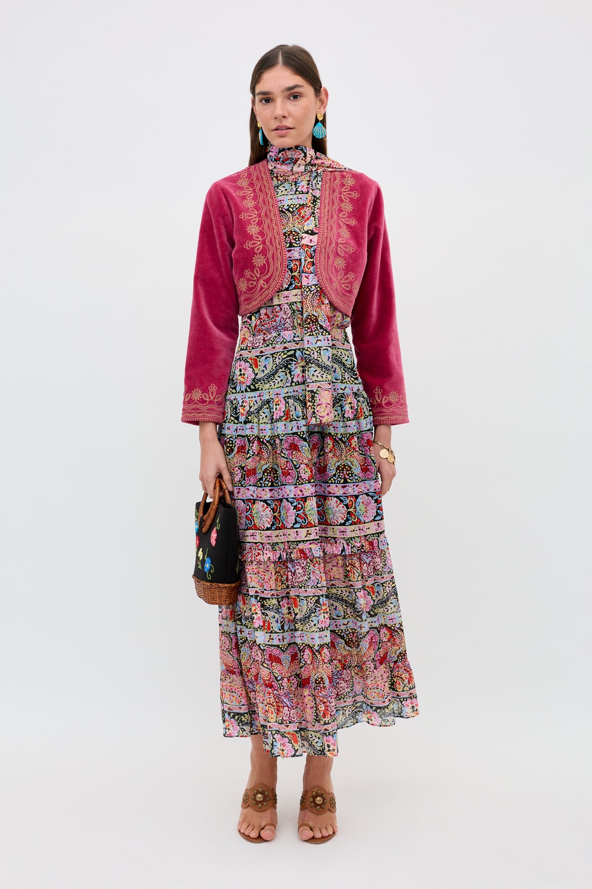 A woman stands against a white background wearing the Abi - Cara Stripe Black, paired with a colorful floral dress, small handbag, brown sandals, and turquoise earrings.