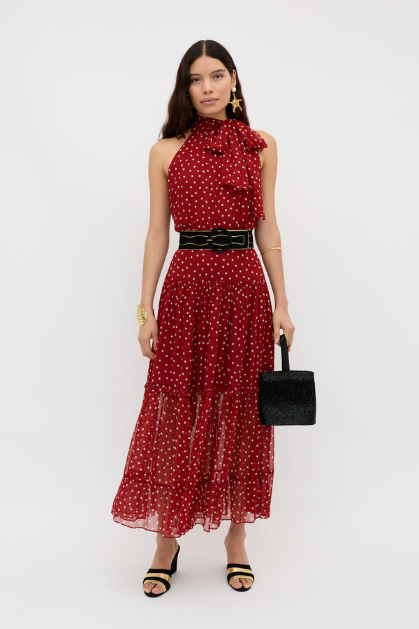 A woman wears the Abi - Layla Dot Red midi dress with a black belt, heeled sandals, gold jewelry, and a small black handbag as she stands against a white background.