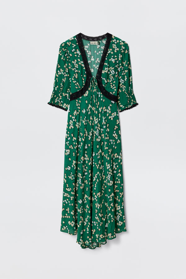 The Amina - City Floral Olive dress features an olive green midi length, short sleeves, and black lace trim at the neckline and cuffs. Its flowy silhouette is adorned with a charming white and yellow daisy print for a vintage tea dress vibe.