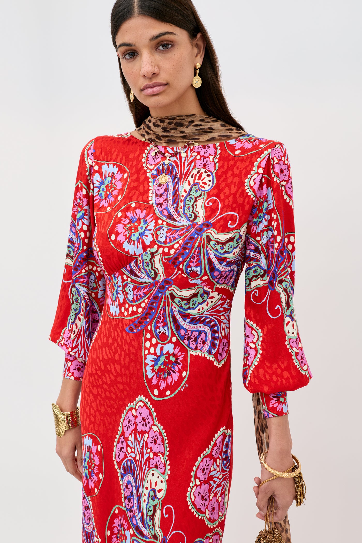 A woman wears the Marni Butterfly Bloom Jacquard Red dress, featuring bold paisley patterns and an animal print collar. She styles it with gold jewelry and has long dark hair.