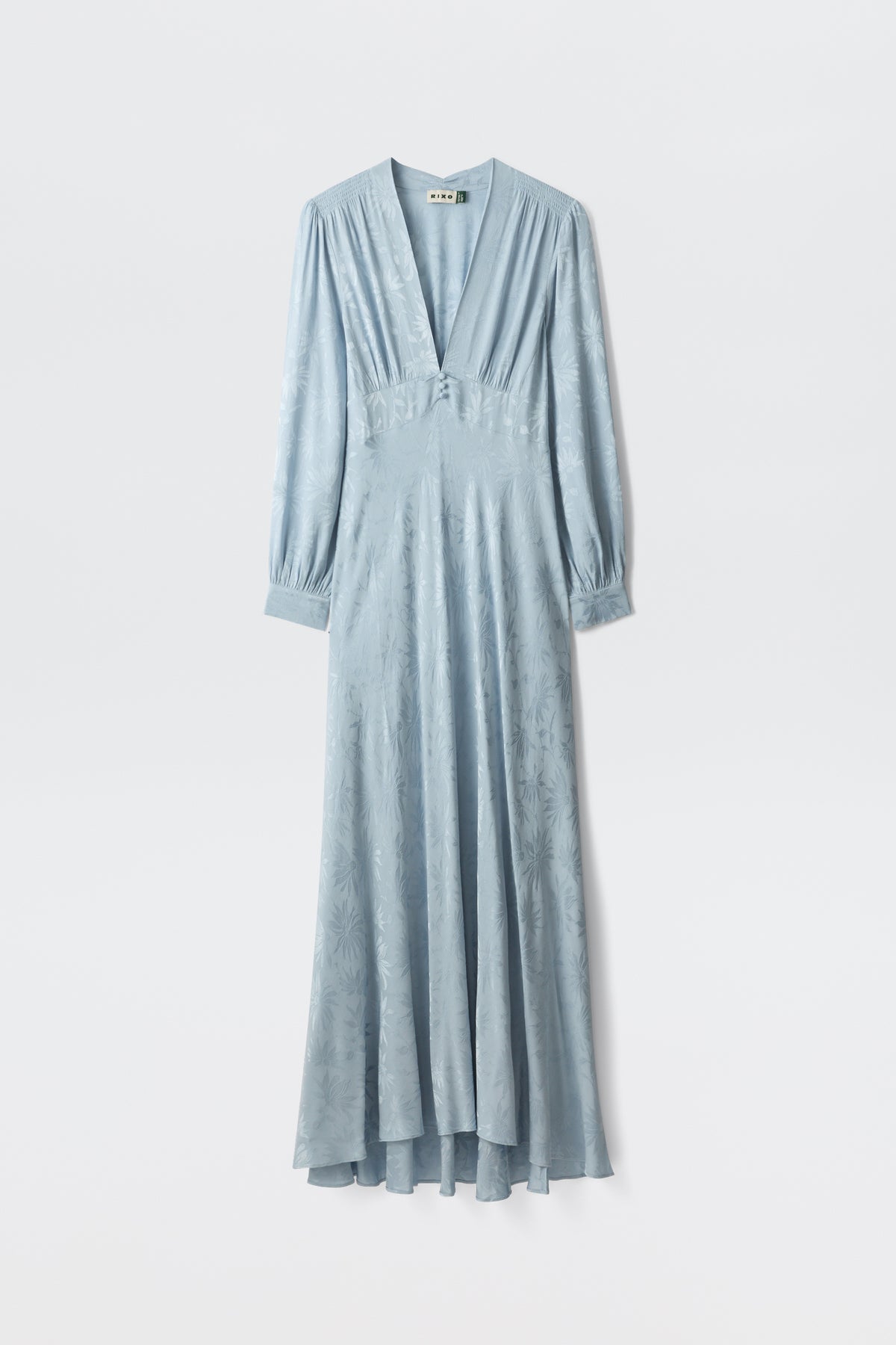 The Emory - Daisy Jacquard Bluebell is a long, light blue satin dress with a deep V-neckline, buttoned-cuff long sleeves, a fitted waist, and a subtle floral pattern, shown on a white background.