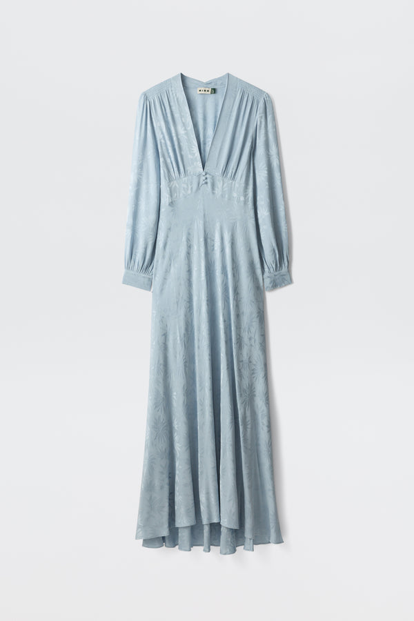 The Emory - Daisy Jacquard Bluebell is a long, light blue satin dress with a deep V-neckline, buttoned-cuff long sleeves, a fitted waist, and a subtle floral pattern, shown on a white background.