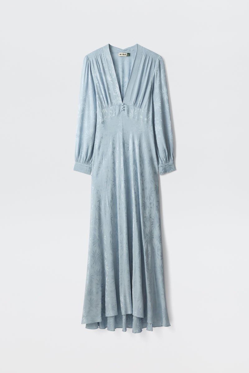The Emory - Daisy Jacquard Bluebell is a long, light blue satin dress with a deep V-neckline, buttoned-cuff long sleeves, a fitted waist, and a subtle floral pattern, shown on a white background.