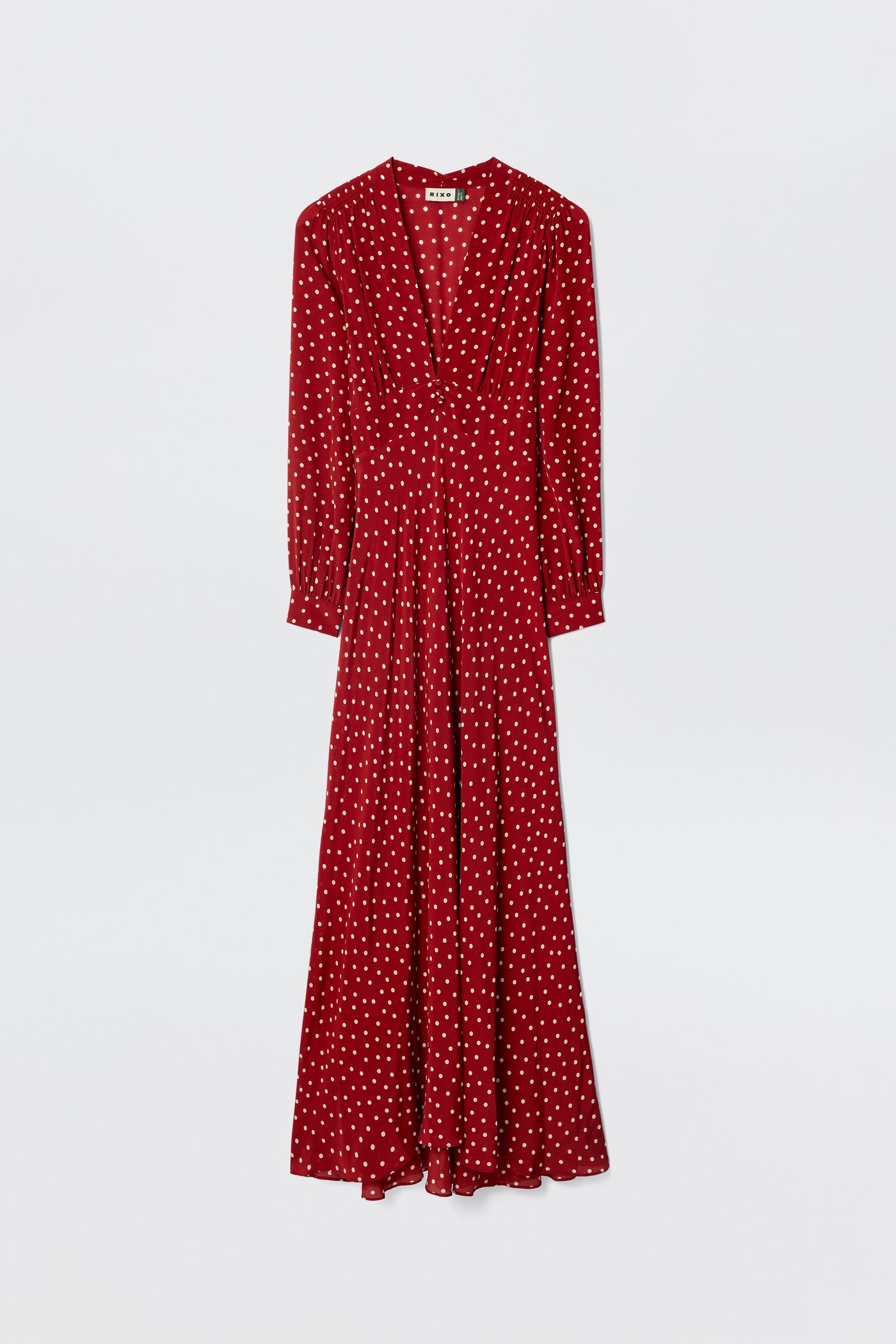 The Emory - Layla Dot Red is a long-sleeved, floor-length gown with white polka dots, a V-neckline, and a flowing skirt, shown against a plain white background.