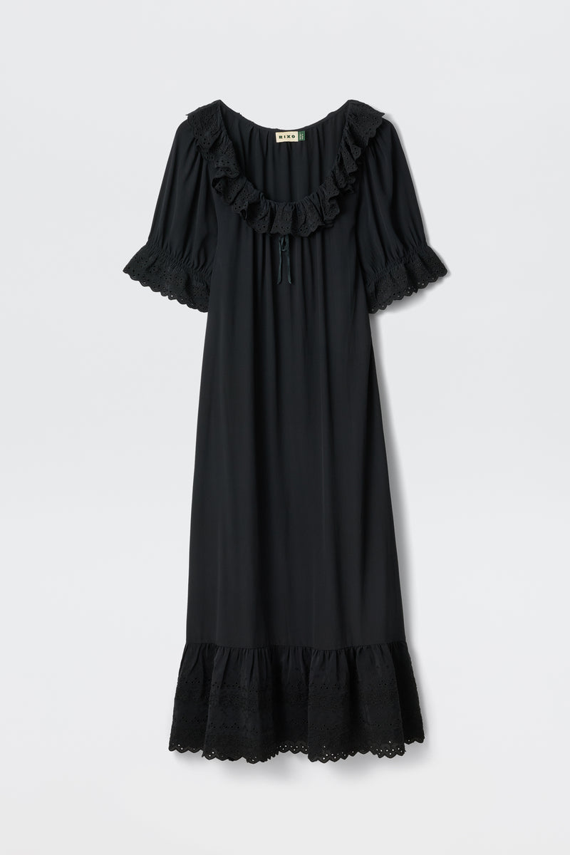 The Aprilia Gracie Embroidery Black is a loose-fitting, knee-length black silk dress with short ruffled sleeves, ruffled neckline and hem, lace details, a tie at the neckline, and vintage sleepwear-inspired elegance.