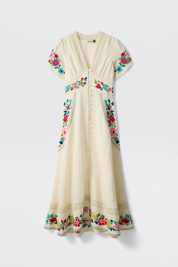 The Novara - Anemone Embroidery Cream is a cream midi dress with short sleeves, a V-neck, and decorative front buttons, featuring colorful floral embroidery on the neckline, sleeves, waist, pockets, and hem.