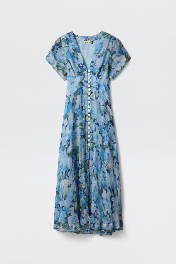 The Novara - Chelsea Floral Blue is an ankle-length, short-sleeve dress with a blue floral pattern, V-neckline, white front buttons, and flowy lightweight fabric for a soft, elegant look.