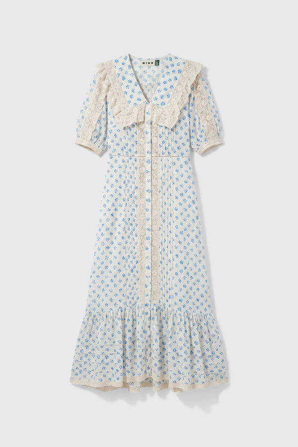 Edina - Seville Floral Cream dress featuring light blue floral patterns, short sleeves, lace trim, a large lace collar, front buttons, and a ruffled hem, displayed on a white background.