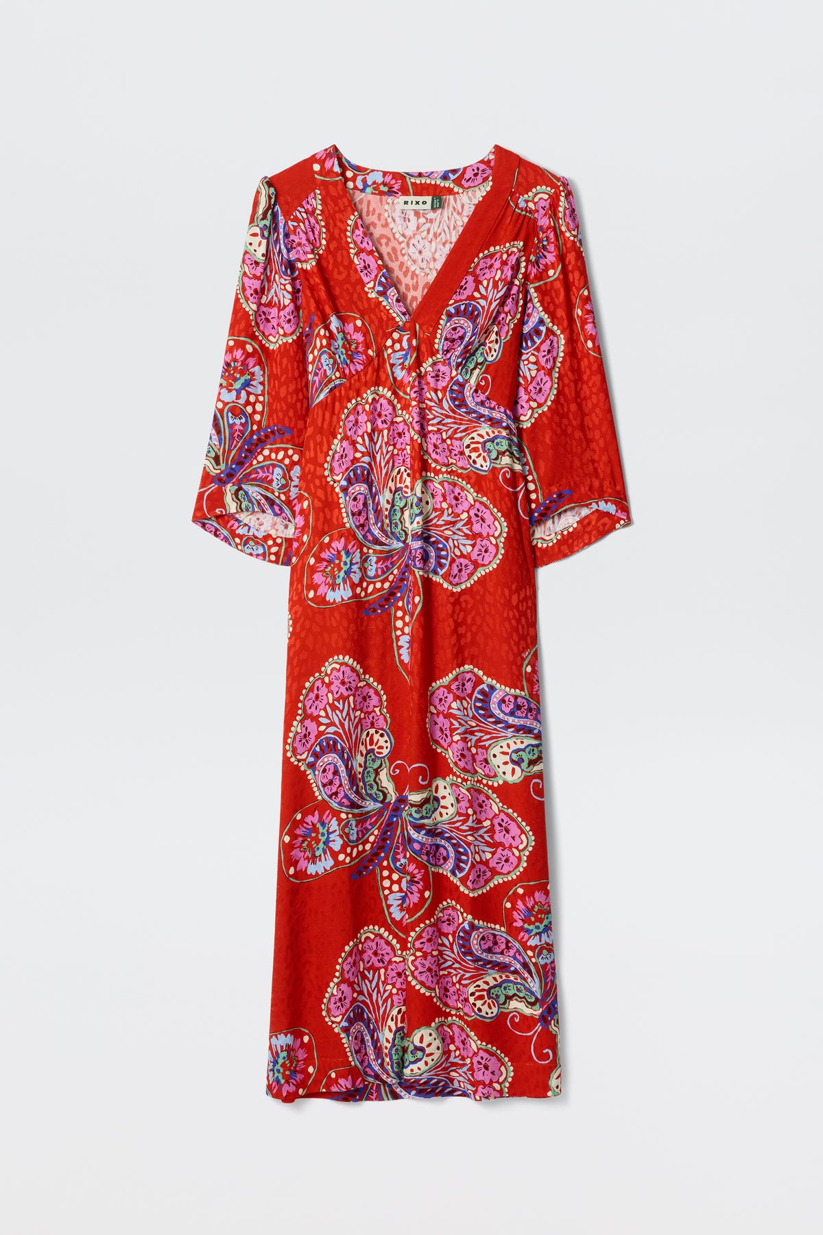 The Dahlia - Butterfly Bloom Jacquard Red is a long red dress featuring a V-neck, three-quarter sleeves, and a vibrant paisley and floral pattern in pink, purple, and blue.