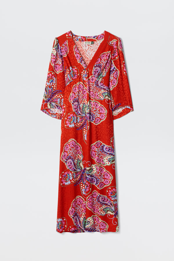 The Dahlia - Butterfly Bloom Jacquard Red is a long red dress featuring a V-neck, three-quarter sleeves, and a vibrant paisley and floral pattern in pink, purple, and blue.
