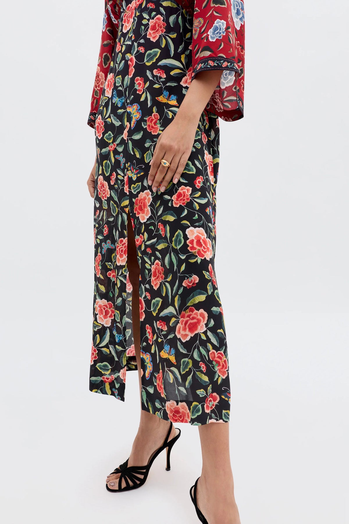 Wearing the Dahlia - Butterfly Mix Black skirt with a front slit in chinoiserie florals, paired with a red floral top and black strappy heels. Only the lower body and one hand with a ring are visible, highlighting this bold transitional piece.