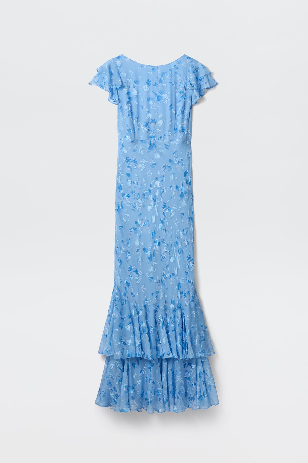 The Ordinia - Ava Devore Blue is a long, light blue dress with a floral pattern, short flutter sleeves, and a layered ruffled hem, shown against a plain white background.