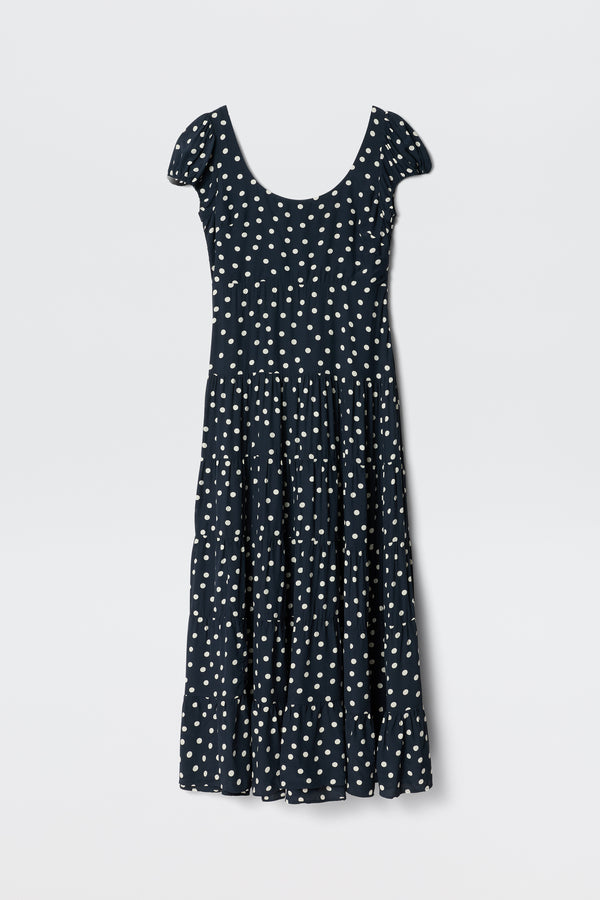 The Remi - Bohemia Spot Deep Navy dress features a scoop neck, white polka dots, short sleeves, and an ankle-length tiered skirt—ideal for summer and shown on a plain white background.