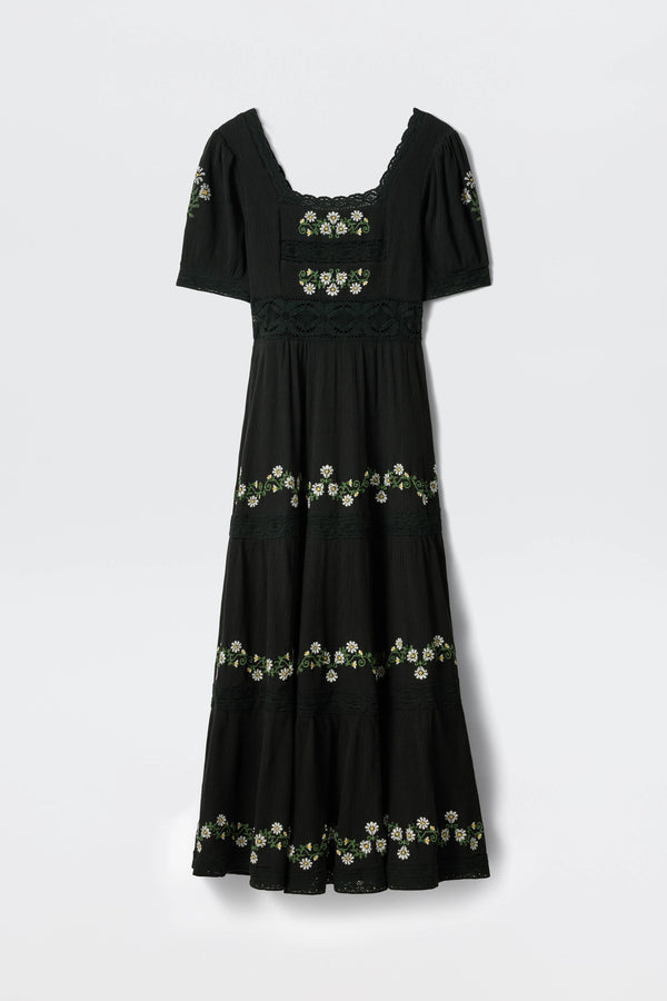 The Philippa - Lilia Embroidery Black is a black, ankle-length, short-sleeve dress with a square neckline and white-and-yellow floral embroidery in horizontal bands across the bodice, sleeves, and skirt.