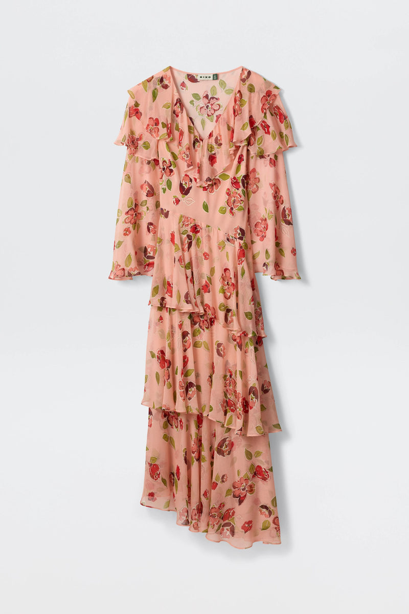 The Loralyn - Kimmie Floral Pink dress is long-sleeved with ruffled layers and an asymmetrical hem, featuring red and green flowers on a light pink background.