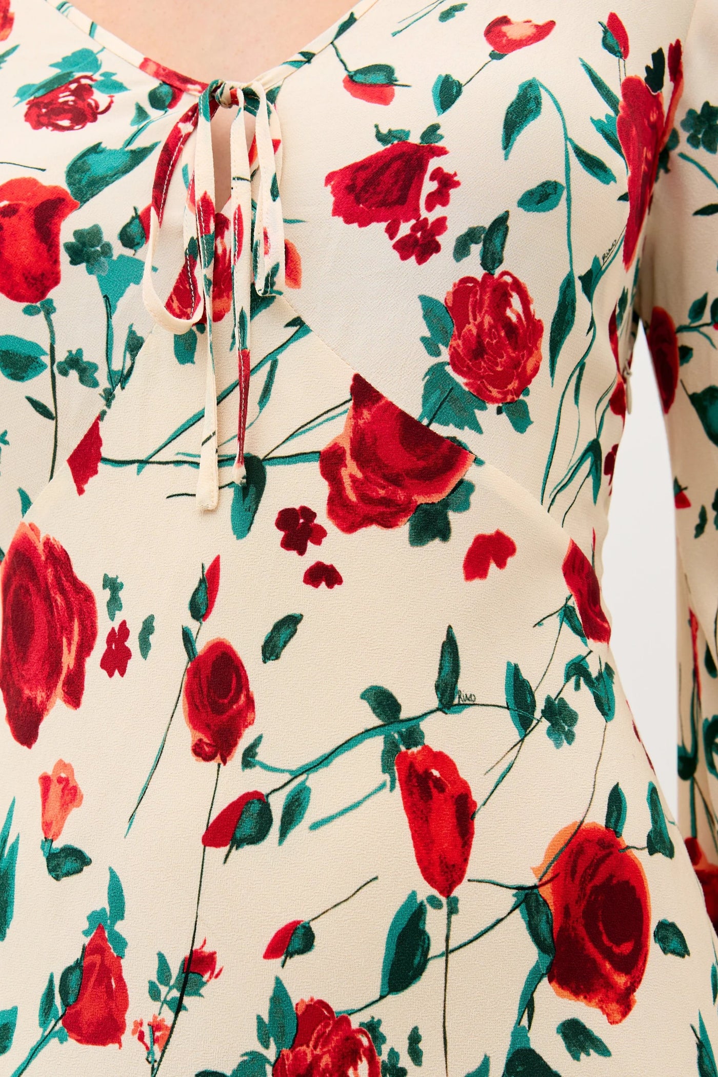 Close-up of the Gwenyth - Claudia Rose Cream dress, showcasing cream fabric with red roses and green leaves, and a V-neckline accented by a small tie detail.